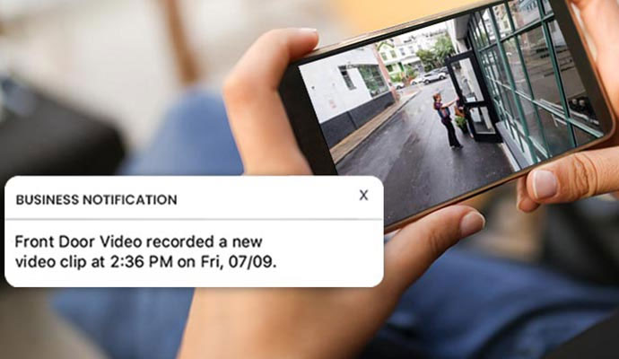 A person viewing a live outdoor security camera feed and a notification pop-up for a recorded video clip on their smartphone